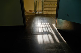 Offene Tür mit Sonnenlicht, das durch ein Fenster auf den dunklen Boden fällt.