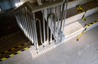 Treppenabsatz mit Metallgeländer, gelb-schwarzem Absperrband und Schattenwurf.