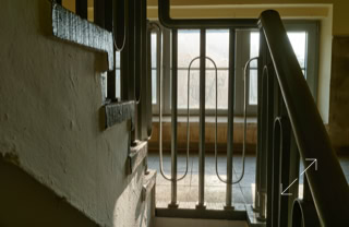 Treppenhaus mit Geländer und Fenster im Hintergrund.