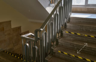 Ein Treppenhaus mit Metallgeländer und gelb-schwarzen Markierungen auf den Stufen, beleuchtet durch ein Fenster im Hintergrund.