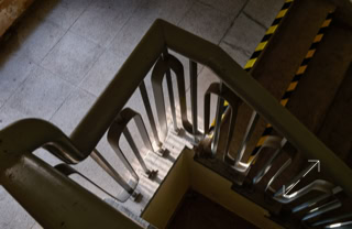Blick von oben auf ein Treppenhaus mit Metallgeländer und gelb-schwarzen Warnstreifen an der Seite.