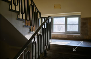 Treppenhaus mit Metallgeländer und einem Fenster, durch das Tageslicht einfällt.
